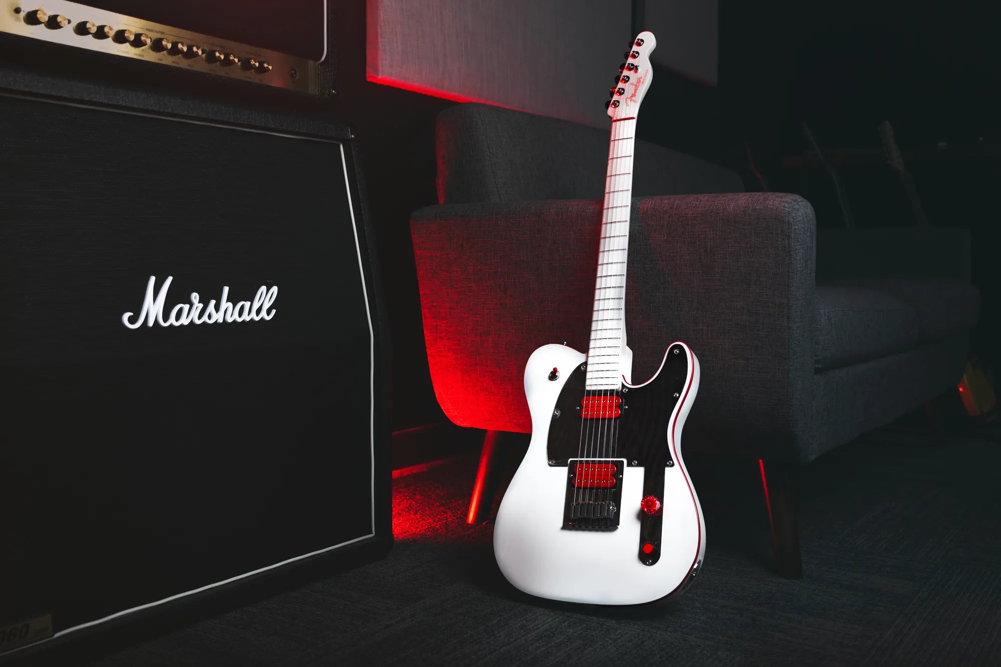 White electric guitar with red accents next to a Marshall amplifier in a dark room.